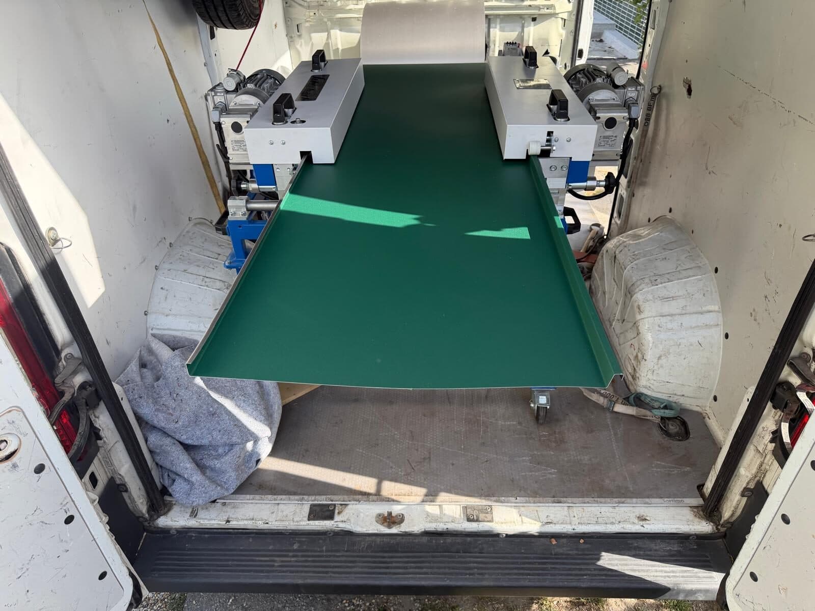 Ein langes grünes Stehfalz-Blech kommt aus der Profilieranlage im Laderaum eines Transporters.